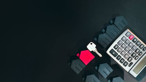 A house-shaped keyring and a calculator on a dark desk.